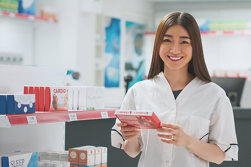 Junge Frau hält in der Apotheke eine Faltschachtel mit Cleanem Label