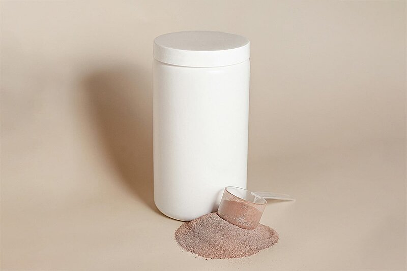 Unbedruckte Dose mit einem Messlöffel und etwas Proteinpulver davor