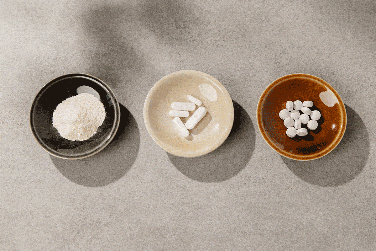 Drei Schälchen auf grauem Untergrund, die immer wieder ihre Position wechseln. Darin befinden sich Tabletten, Kapseln und Pulver