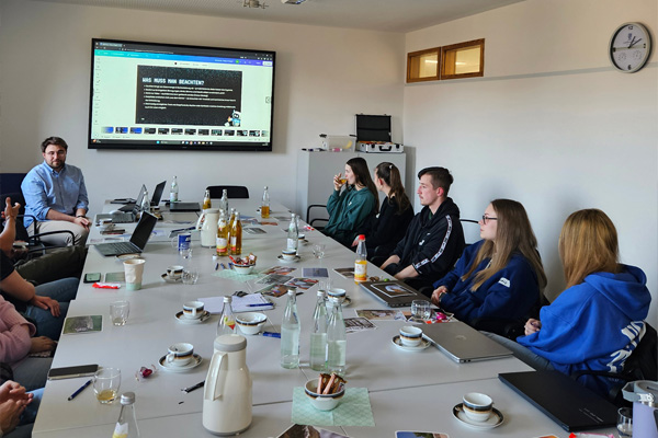 Auszubildende an einem Konferenztisch, während sie einen Vortrag zum Thema Deep Fake hören