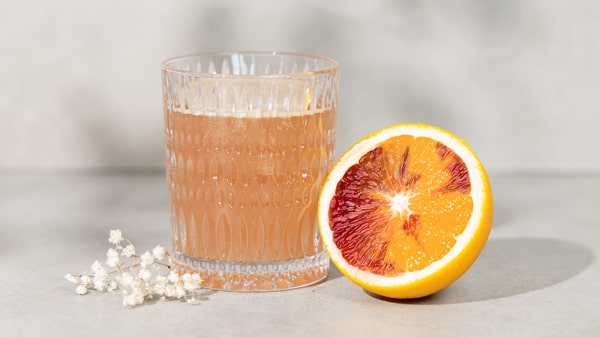 Blass orangener Frauengesundheitsdrink mit einer angeschnittenen Blutorange daneben