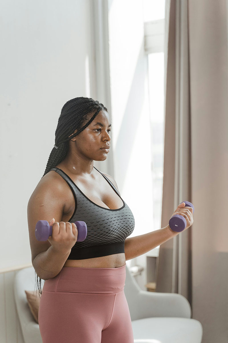 Junge Frau hat zwei Pilateshanteln in der Hand und macht ein Workout