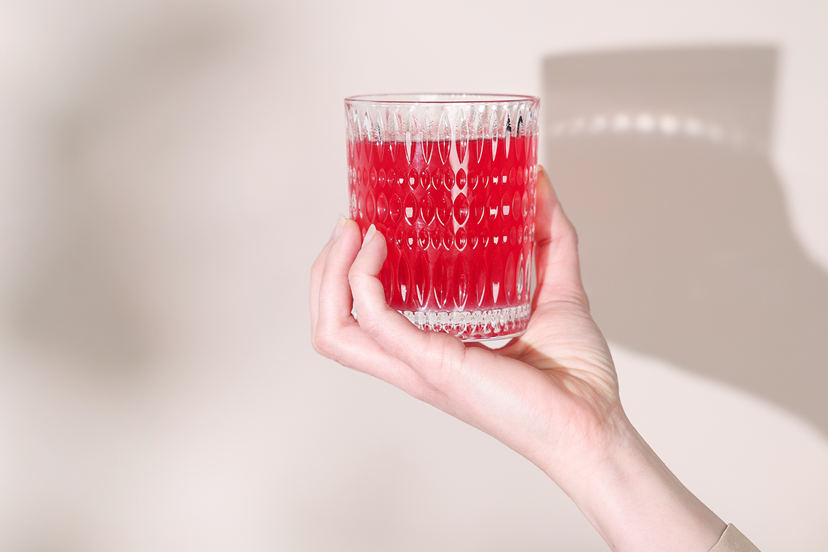 Vor einfarbigem Hintergrund wird ein Glas voll rotem Isodrink von einer Hand gehalten