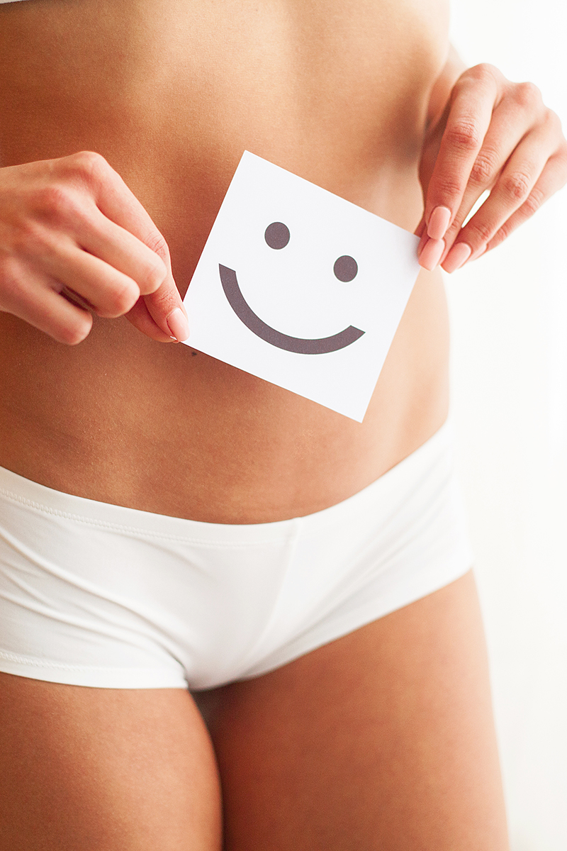 Zwei Hände halten einen Zettel mit smiley vor einen Bauch