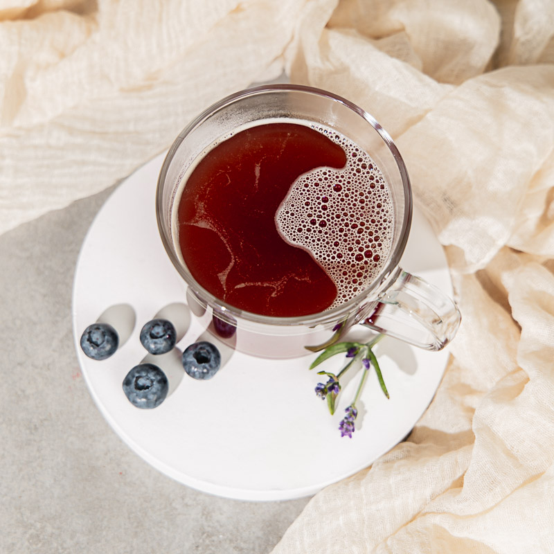 Tee zur Frauengesundheit von oben fotografiert, dazu Beeren, Lavendel und beiger Stoff