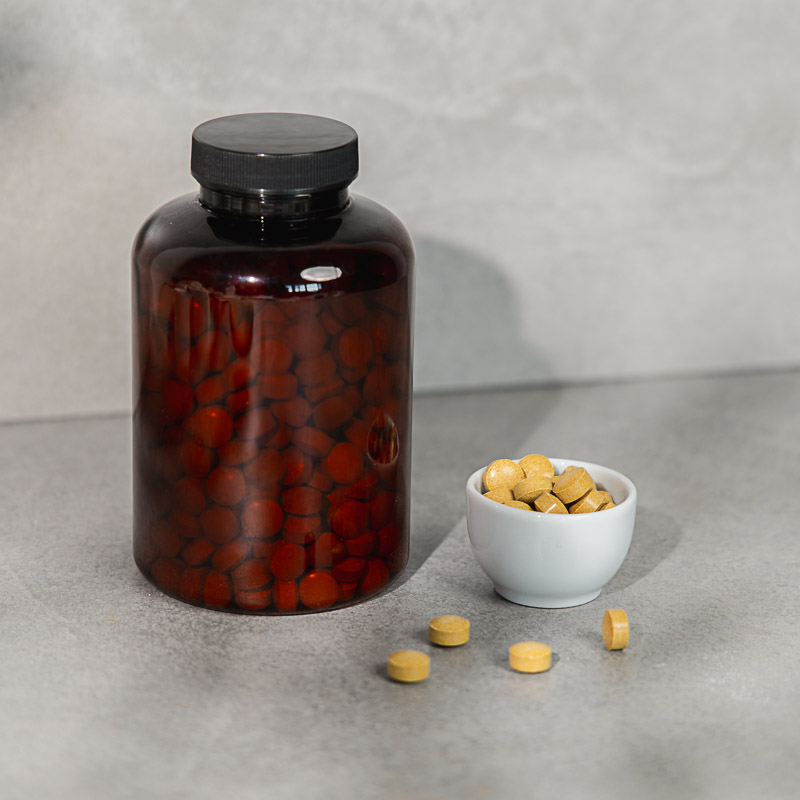 Ockerfarbene Femme Fertile Tabletten zur Unterstützung der Frauengesundheit in einem weißen Schälchen, daneben ein braunes Glas mit Schraubdeckel
