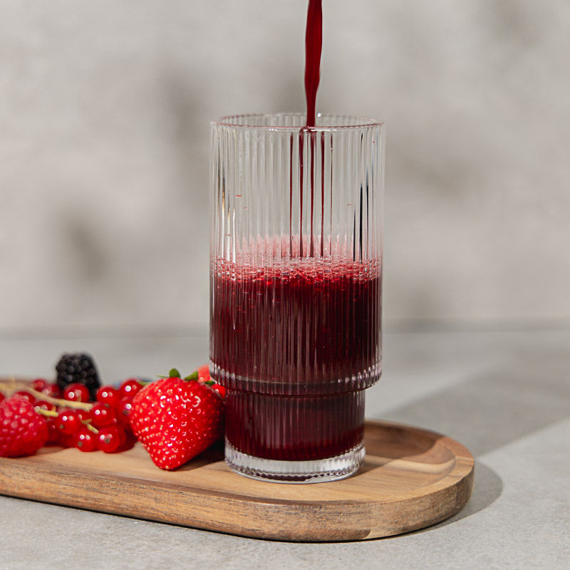 Roter Immunsmoothie wird in ein Glas gegossen, daneben liegen rote Beeren
