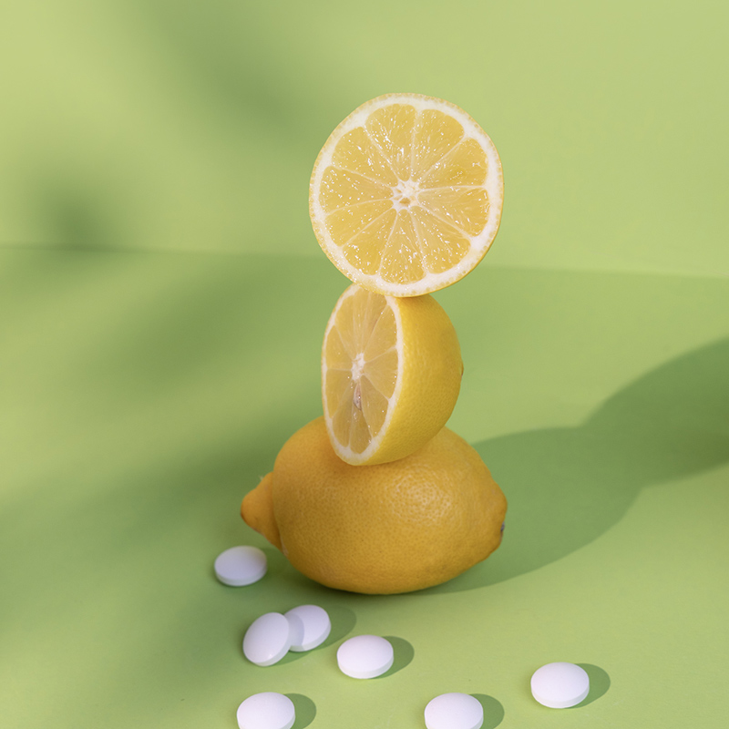 Sour Power Tabletten liegen auf grünem Hintergrund, dahinter ein Turm aus angeschnittenen Zitronen