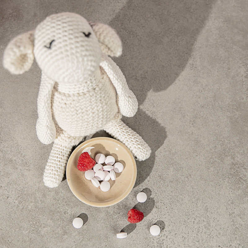 Kindertabletten in einer Schale vor einem Kuschelschaf, Blick vo oben, dazu Himbeeren