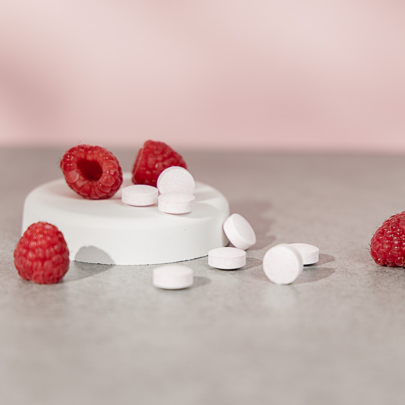 Himbeeren und Tabletten auf einem kleinen, weißen Posest vor rosa Hintergrund