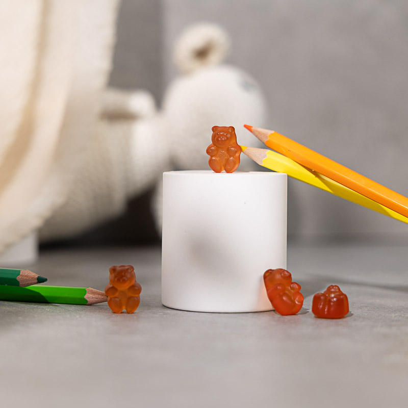 Gummies liegen zwischen Stiften und einem Kuscheltier auf einem weißen Podest