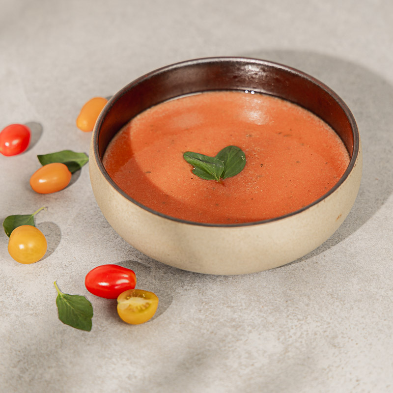 Proteinsuppe Tomate zum Gewichtsmanagement in einer Schale, daneben bunte Tomaten