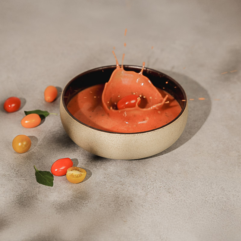 Tomatensuppe zum Gewichtsmanagement in einer Schale. Eine Tomate fällt hinein und verursacht Spritzer