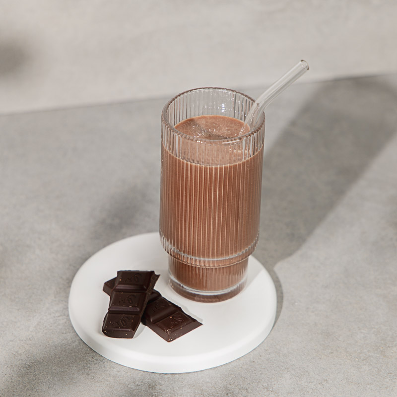 Mahlzeitenersatz Shake in einem hohen Glas, daneben 2 Rippen Schokolade