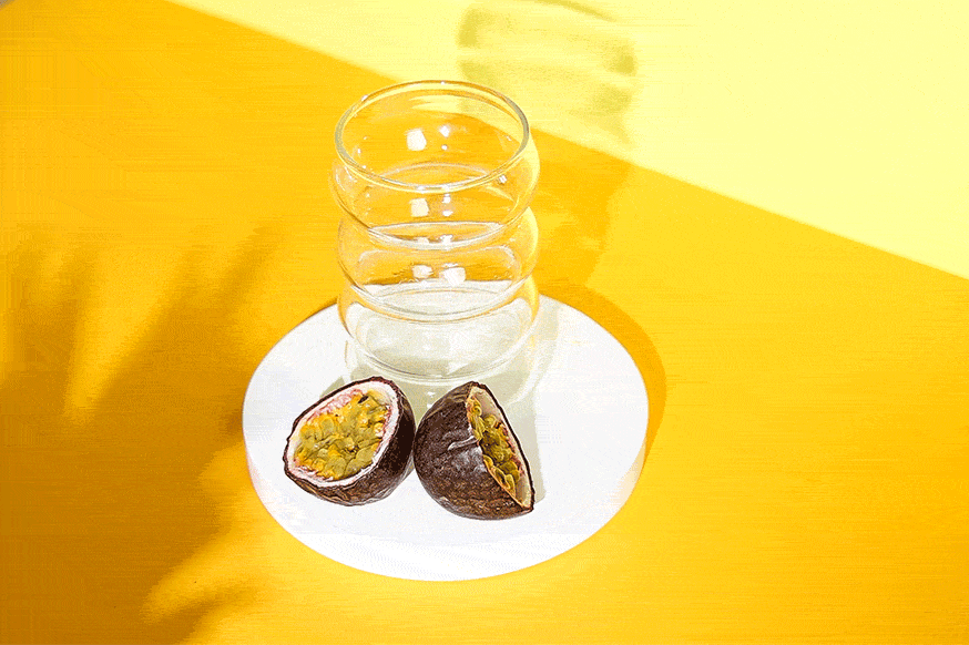 Mellow Yellow Drink ird in ein Glas gegossen. Davor eine aufgeschnittene Maracuja