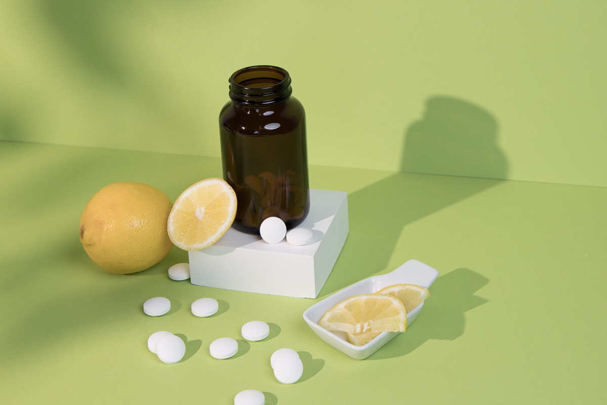 Braunglas umgeben von Zitronen und Lutschtabletten vor grünem Hintergrund