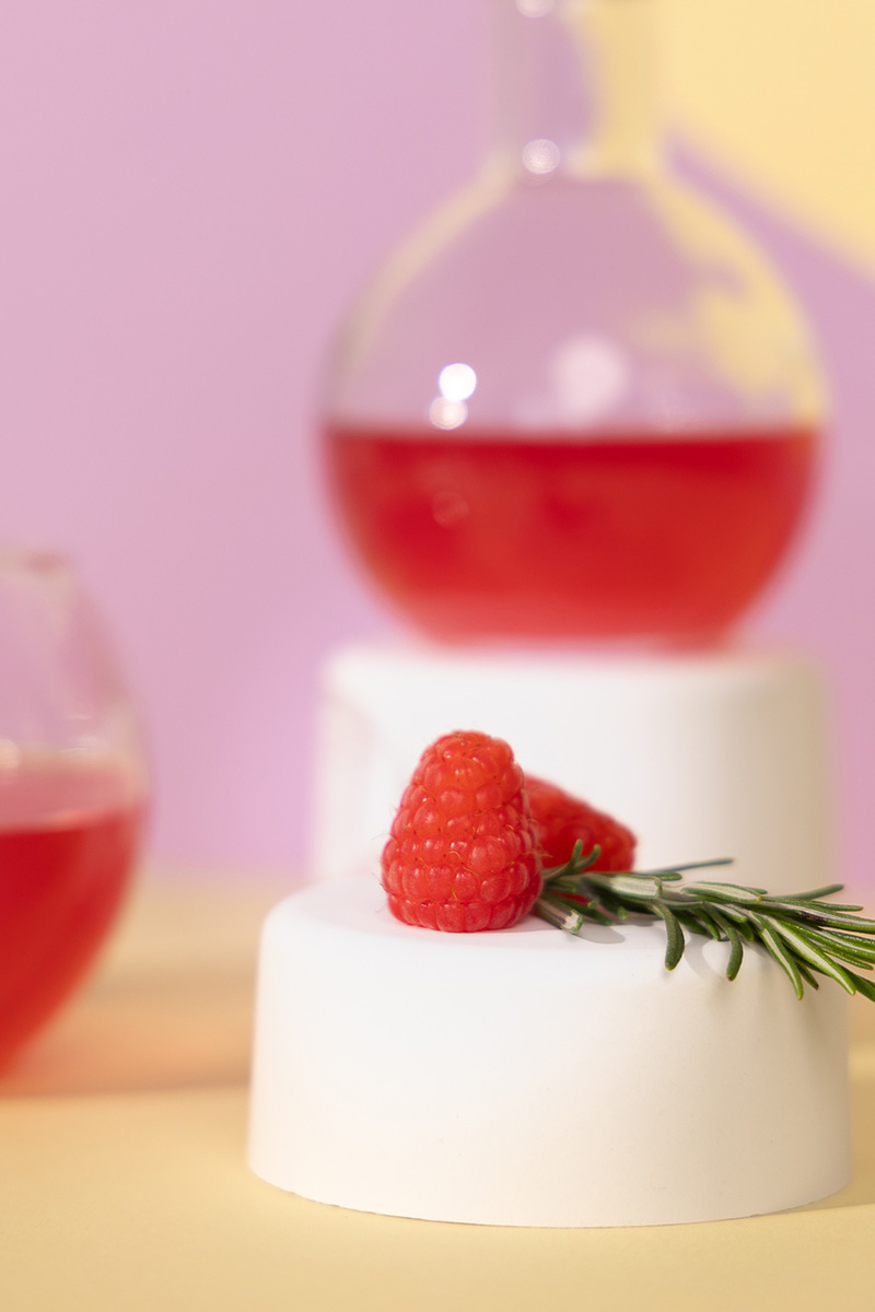 Himbeeren liegen auf Podest mit Getränk im Hintergrund